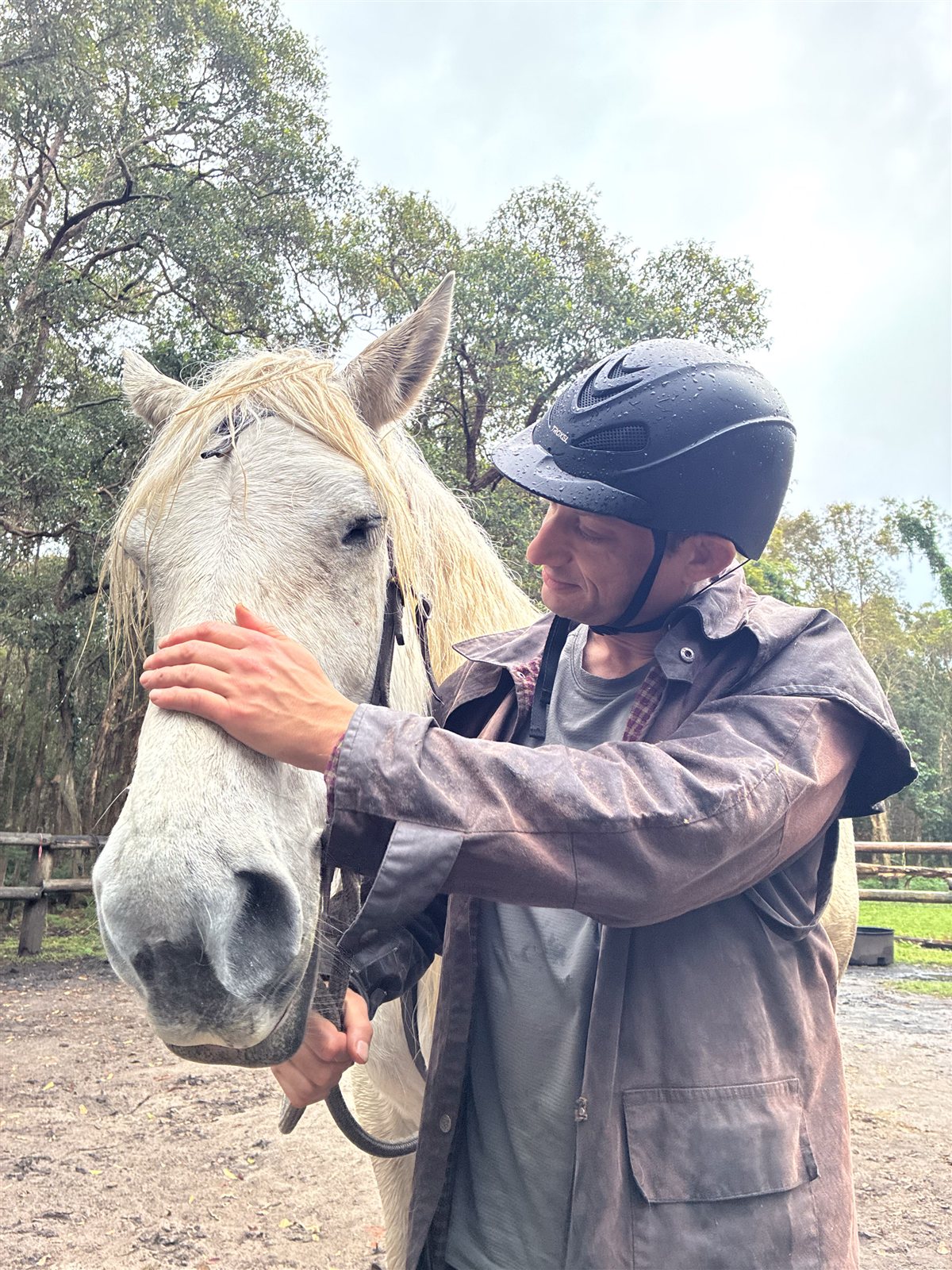 Active Outings founder Benjamin wearing a helmet and gently stroking Pam, a white horse
