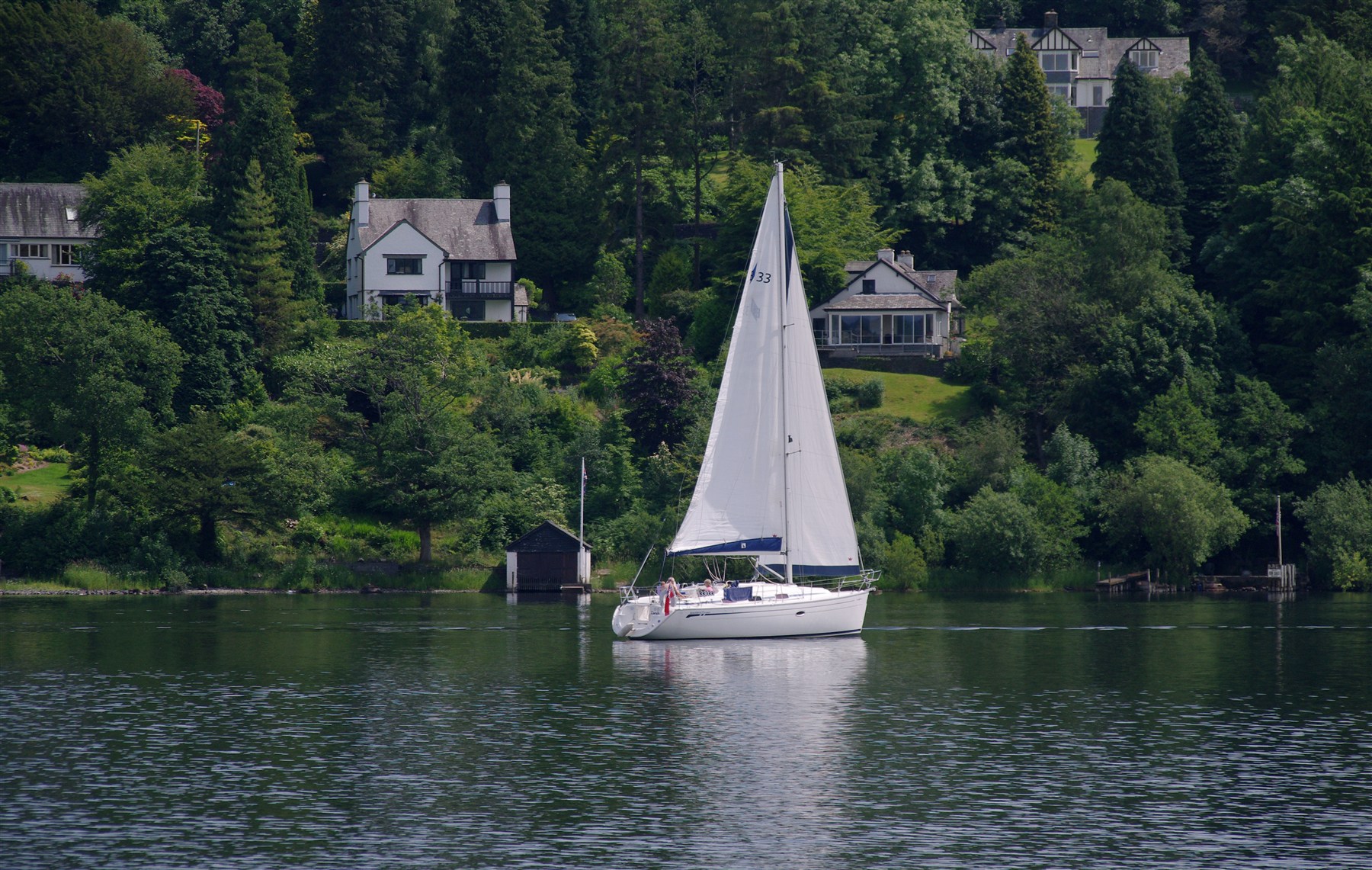 A whole white sailing boat gliding gently across a calm lake, with its sail and hull in view